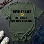 Green Comfort Colors t-shirt with text 'Sorry I'm late, my Frenchie was being dramatic' on a dark surface with shoes and jeans.