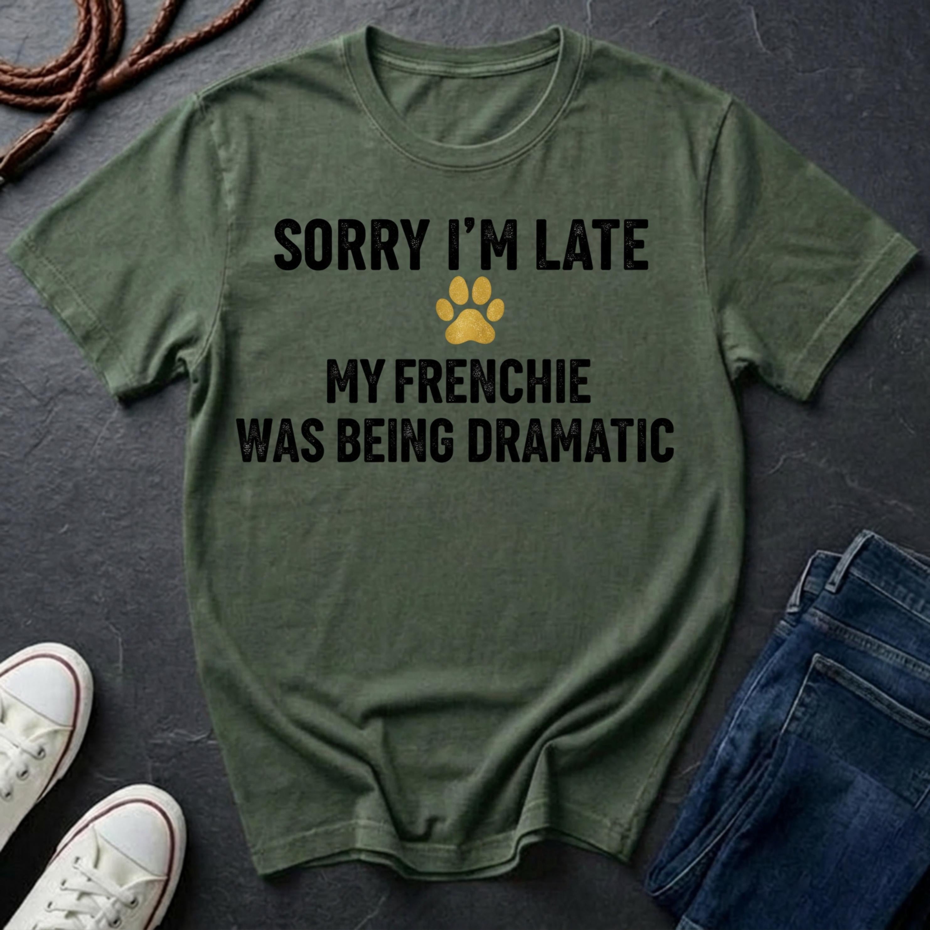 Green Comfort Colors t-shirt with text 'Sorry I'm late, my Frenchie was being dramatic' on a dark surface with shoes and jeans.