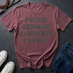 Maroon Comfort Colors t-shirt with 'PROUD GERMAN SHEPHERD PARENT' text on a dark surface with shoes and jeans.