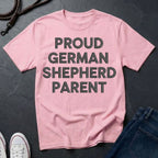 Pink Comfort Colors t-shirt with 'Proud German Shepherd Parent' text on a dark surface with jeans and shoes.