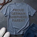 Blue Comfort Colors t-shirt with 'PROUD GERMAN SHEPHERD PARENT' text on a dark surface with shoes and jeans.