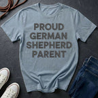 Blue Comfort Colors t-shirt with 'Proud German Shepherd Parent' text on a dark surface with shoes and jeans.
