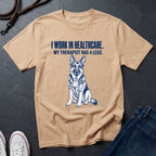 Beige Comfort Colors t-shirt with a dog graphic and text on a dark surface with shoes and jeans.