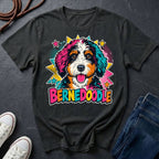 A black short-sleeve comfort colors Tee featuring a colorful pop-art Bernedoodle dog graphic with the word 'BERNEDOODLE' in bright multicolor letters.