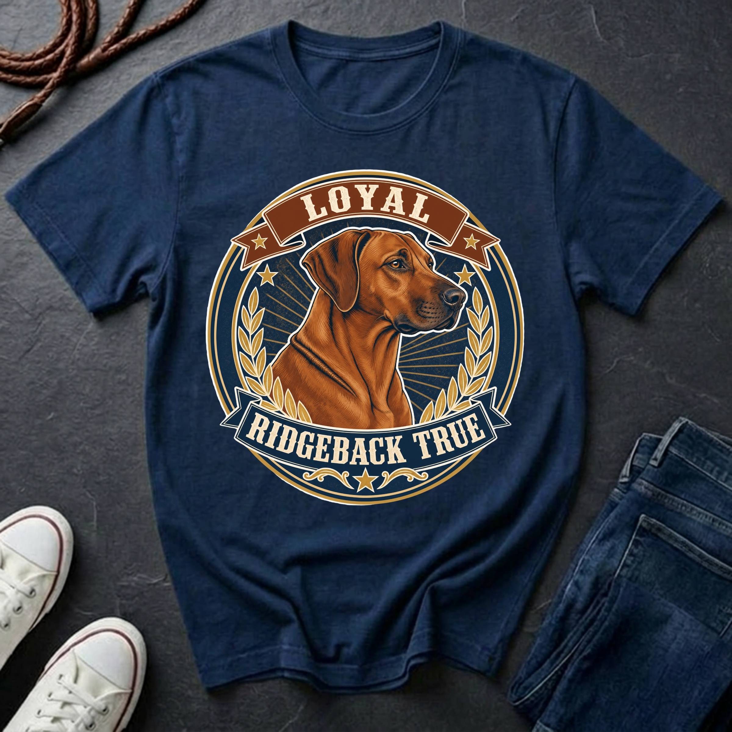 A navy blue graphic t-shirt laid flat on a dark slate surface, featuring a circular design with a Rhodesian Ridgeback dog and the text 'LOYAL RIDGEBACK TRUE'. White sneakers and a pair of blue jeans are styled around the shirt, with a coiled rope in the top-left corner.