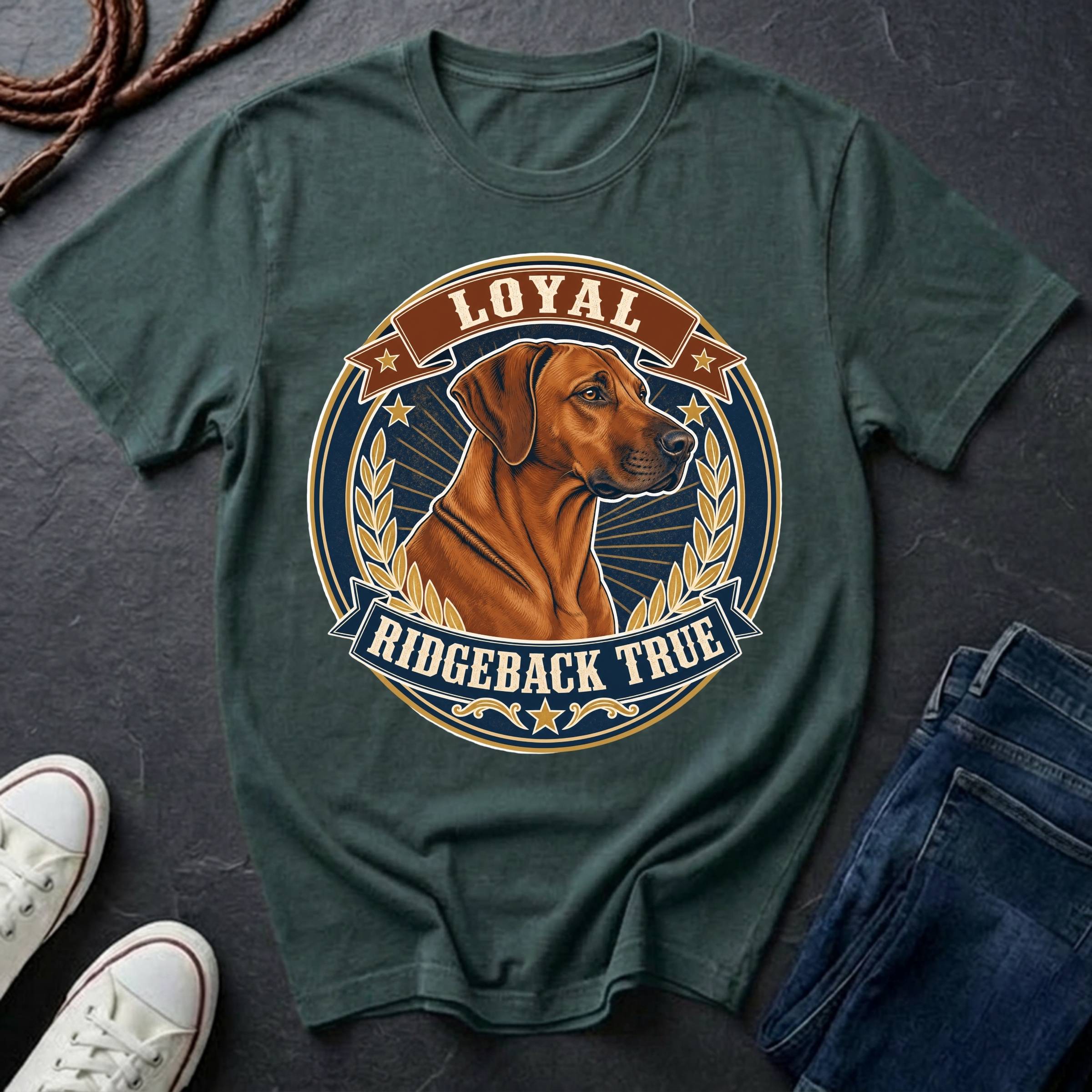 A blue spruce graphic t-shirt featuring a Rhodesian Ridgeback dog illustration inside a circular badge with the text 'LOYAL RIDGEBACK TRUE'. The shirt is styled in a flat-lay arrangement on a dark slate surface, accompanied by white sneakers, a coiled rope, and a pair of blue jeans.