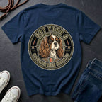 A navy blue graphic t-shirt featuring a Cavalier King Charles Spaniel dog illustration inside a circular emblem with the text 'GOT YOUR 6 CAVALIER KING CHARLES 6'. The t-shirt is styled in a flat-lay arrangement on a dark slate background, accompanied by white sneakers, a coiled rope, and blue jeans.