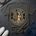 A dark pepper t-shirt laid flat on a dark slate background, styled with white sneakers, blue jeans, and a leather strap. The back of the shirt features a large circular graphic of a Cavalier King Charles Spaniel dog inside a seal with the text 'GOT YOUR 6 CAVALIER KING CHARLES 6'.