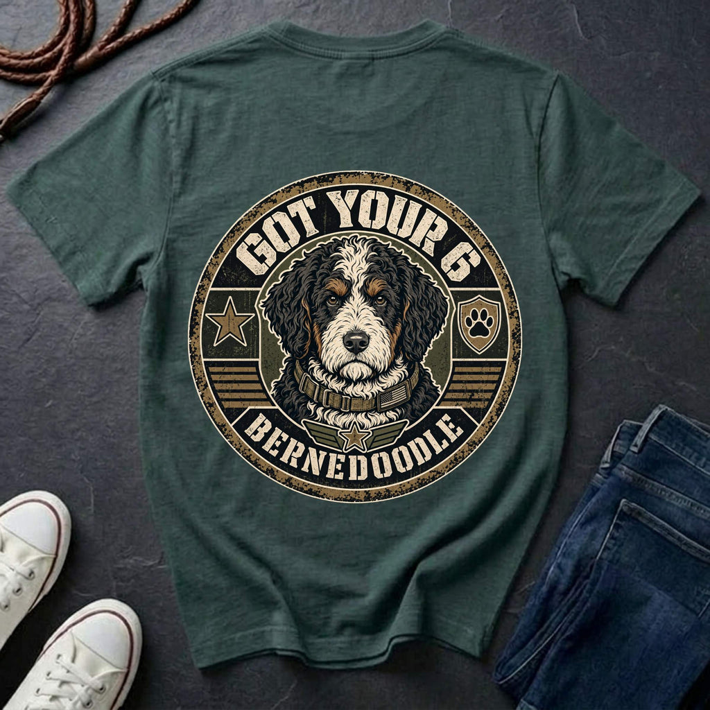 A blue spruce graphic t-shirt laid flat on a dark slate surface, styled with white sneakers, blue jeans, and a rope. The back of the shirt features a large circular graphic of a Bernedoodle dog with the text 'GOT YOUR 6 BERNEDOODLE'.