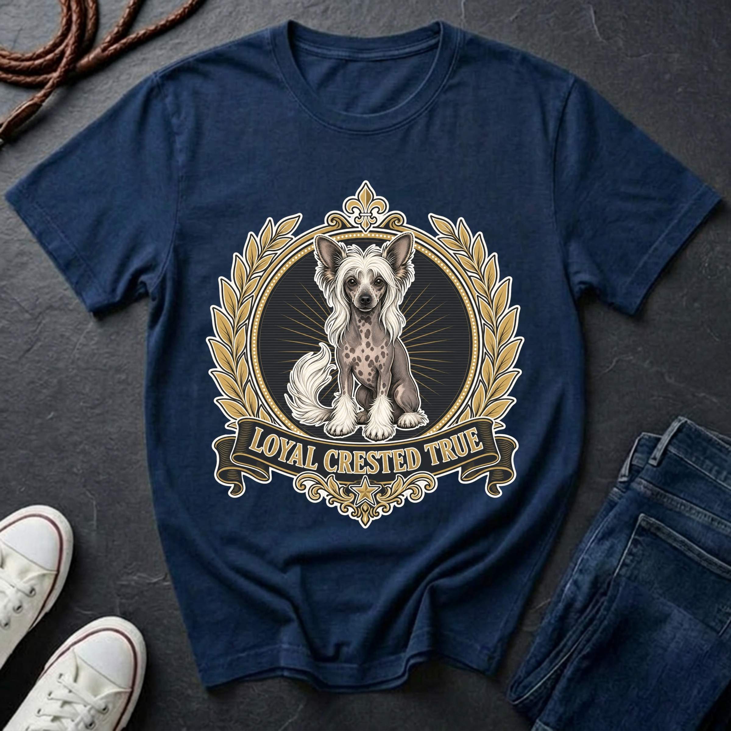 A navy blue graphic t-shirt featuring a detailed illustration of a Chinese Crested dog inside an ornate gold and beige laurel wreath, with a banner reading 'LOYAL CRESTED TRUE'. The t-shirt is styled in a flat-lay arrangement on a dark slate surface, accompanied by white sneakers, a coiled rope, and blue jeans.