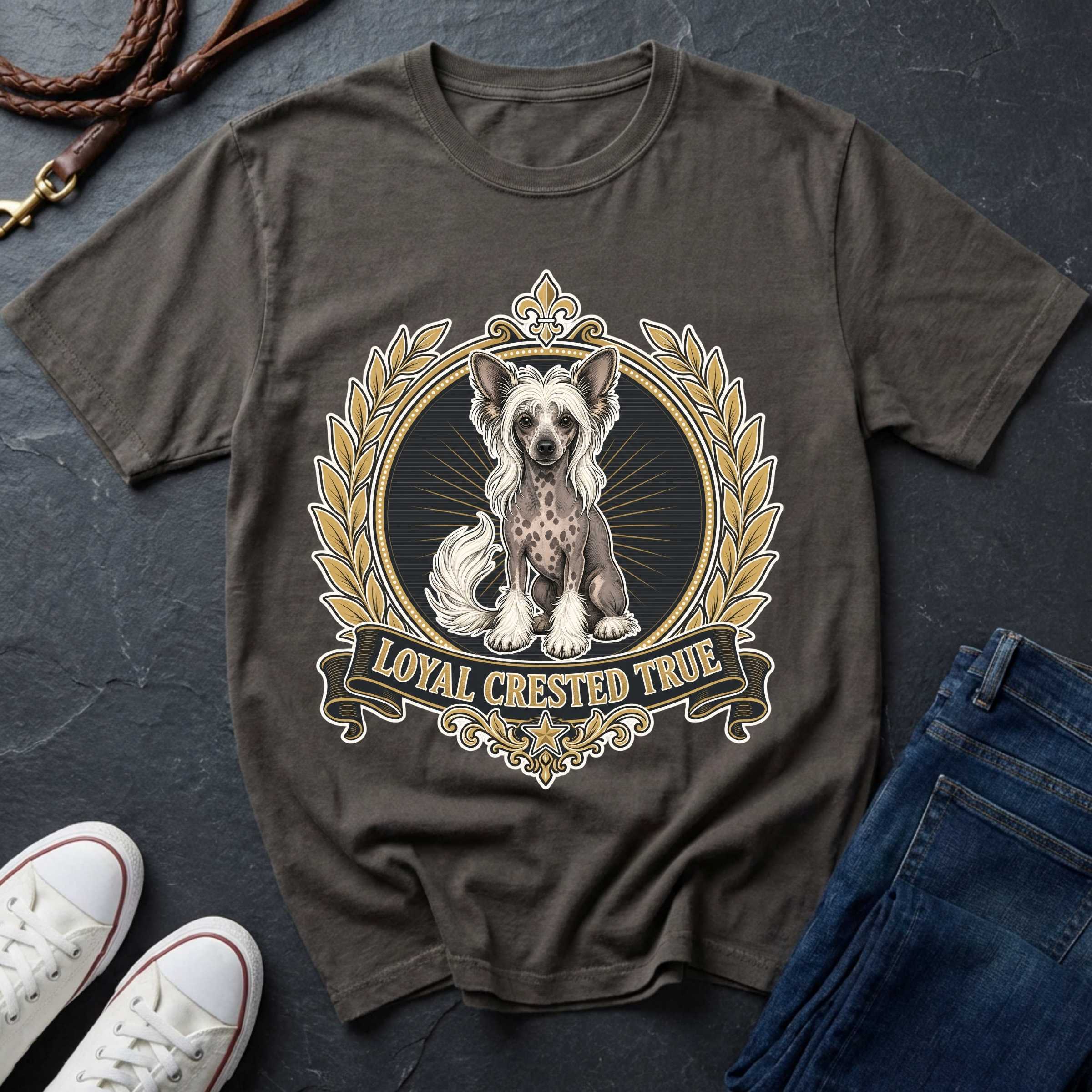 A pepper graphic t-shirt featuring a Chinese Crested dog illustration inside a gold and black decorative crest with the text 'LOYAL CRESTED TRUE'. The shirt is styled in a flat lay with blue jeans, white sneakers, a leather harness, and a dark slate background.