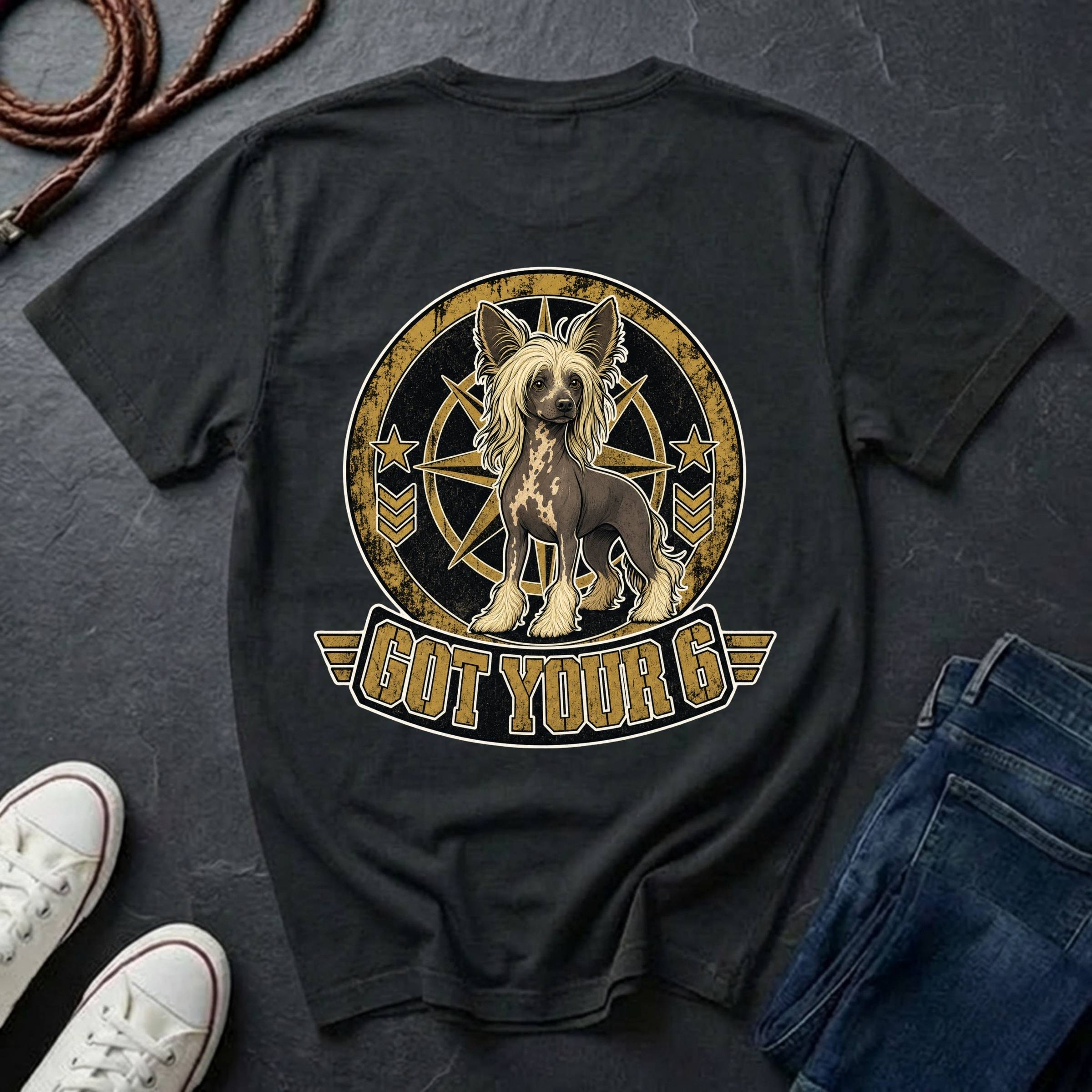 A black graphic t-shirt laid flat on a dark gray slate background, styled with a pair of blue jeans, white sneakers, and a brown leather strap. The t-shirt features a large circular graphic of a Chinese Crested dog with the text 'GOT YOUR 6' below it.