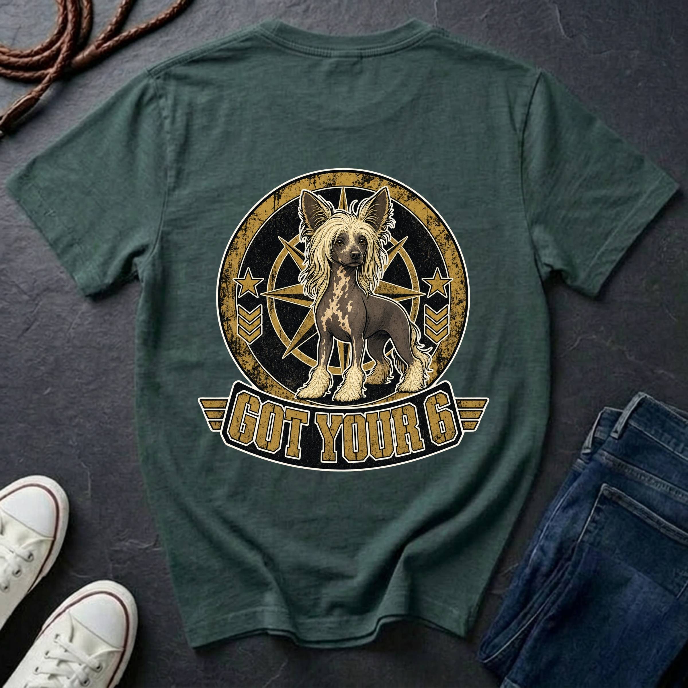 A blue spruce graphic t-shirt laid flat on a dark slate background, styled with a pair of blue jeans, white sneakers, and a coiled rope. The back of the shirt features a large circular graphic of a Chinese Crested dog inside a compass design with the text 'GOT YOUR 6' below it.