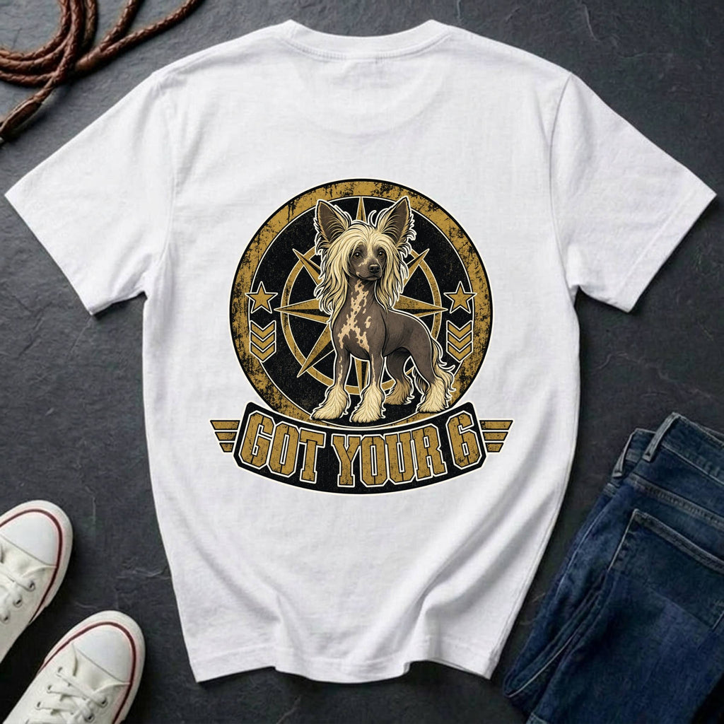 A white short-sleeve graphic T-shirt laid flat on a dark textured surface, styled with a pair of blue jeans, white sneakers, and a coiled rope. The shirt features a large circular graphic of a Chinese Crested dog inside a compass design with the text 'GOT YOUR 6' below.